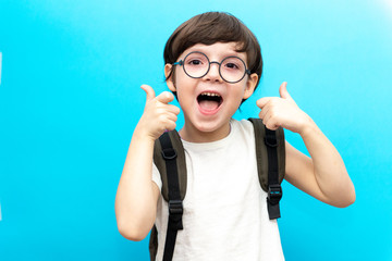 For the first time to school. Happy smiling boy with thumb up. A child from elementary school in uniform. Toddler indoors on a blue background. Funny baby - Powered by Adobe
