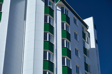 facade of a new multistory building with white and green metal siding, many Windows