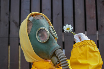 portrait of a human in a gas mask and in a yellow protective suit who holds a white flower in his hand