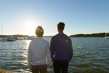 Fototapeta premium Rear view of young multi ethnic couple holding hands together at the pier outdoors