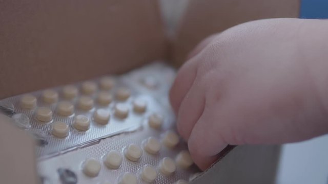 Kid plays with scattering medicine drugs. Toddler touches pills without parent control. Dangerous situation.