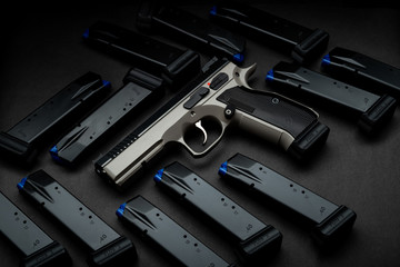Modern brown pistol among ammunition clips on a dark back Short-barreled weapons for sports and...