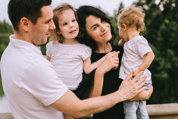 Handsome young father and beautiful mother in sunny summer nature playing with their cute small childrens
