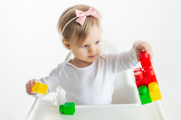 Nursery kid plays with educational toys in classroom sitting at the table in baby chair. Cute little girl playing colorful construction blocks. White background.