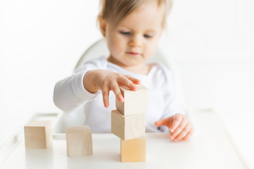 Baby girl playing with wooden cubes by left hand. Playing toddler isolated on white background. Games for kids, preschool education. Close up, selective focus