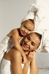 Fototapeta na wymiar A young caucasian woman with his daughter on a bed at home in the morning, wearing in towel play and drink a milk
