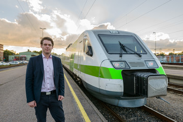 Young handsome businessman standing in front of train at railway station