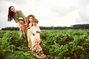 Beautiful young caucasian mother with children in a linen dress with a basket of strawberries...