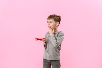 Surprised little boy with flashlight on color background