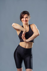 A beautiful sports girl in black sportswear is doing a warm-up before practicing sports at the studio. The concept of a healthy lifestyle. Athletic woman stretches her arms before gym workout.
