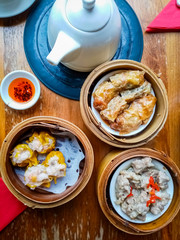 Top View of Delicious Chinese Dim Sum in Bamboo Steamer with Tea Pot and Chili Oil.