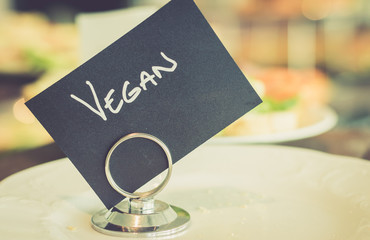 Black vegan sign with handwriting on a clip with blurred food in the background