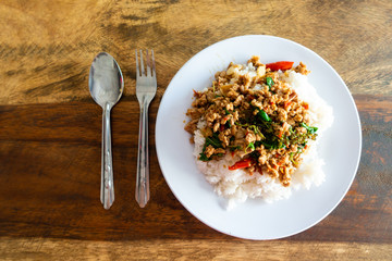 Rice topped with stir-fried pork and basil in a white dish.