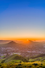 Fototapeta na wymiar Setting Sun over Mountain Peaks, City, Town, from View 
