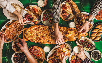 Fototapeta na wymiar Muslim Ramadan iftar family dinner. Flat-lay of peoples hands over table with Middle East food. Dates, kebab, flatbread, pide, borek, sweet, salad over table, top view. Ramazan fasting Turkish cuisine
