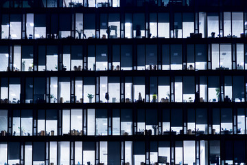 Office Building At Night. Late night at work. Glass curtain wall office building. Office building exterior in the late evening with interior lights on. Evening facade of an office building