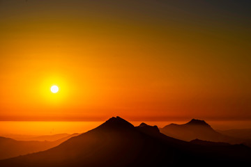 Fototapeta na wymiar Setting Sun over Silhouetted Mountains, Layer of Fog 