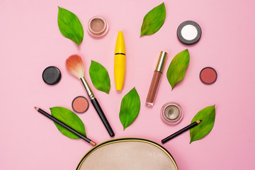 Decorative cosmetics on a pink background next to a beige cosmetic bag and green fresh leaves. The concept of natural cosmetics for make up