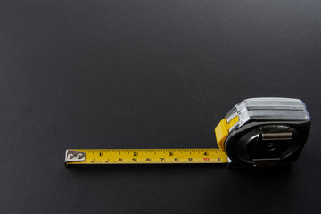 Flexometro o metro color plata con la cinta metrica amarilla sobre un fondo de color negro