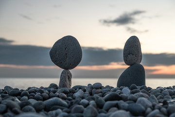 Summer is coming soon in a pandemic. Deserted city beach on the Black Sea. Sculptures of stones, a symbol of people. Stone people. Imitation of lovers. Art installation from pebbles. Meditation at sea