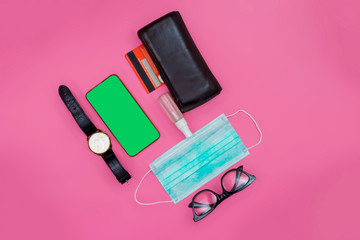 Mockup mobile phone with facial masks, wristwatch, credit card, wallet and Alcohol Mini Hand Sanitizer Spray on a pink workspace