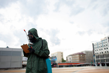 disinfection of the city from viruses and infections, a sanitary worker in a protective suit and a respirator cleans the street with a chemical agent