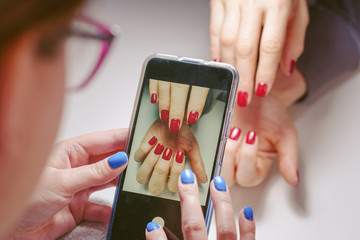 Unknown caucasian woman young female taking photo of nail polish finger nails after beauty manicure of another girl using smart phone making photograph manicurist taking photo of client's close up