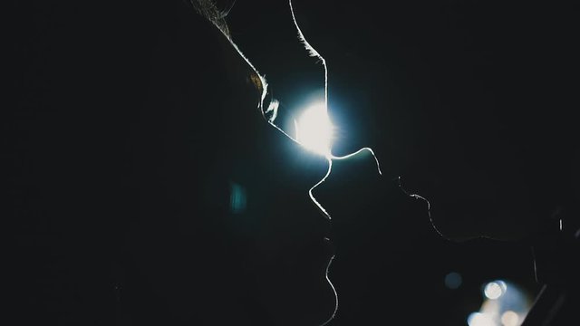 CU, slow motion: black silhouettes of amorous young couple profiles looking at each other against bright light disk in dark space extreme close view