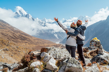 Couple rising arms rejoicing Everest Base Camp trekking route near Dughla 4620m. Backpackers left...