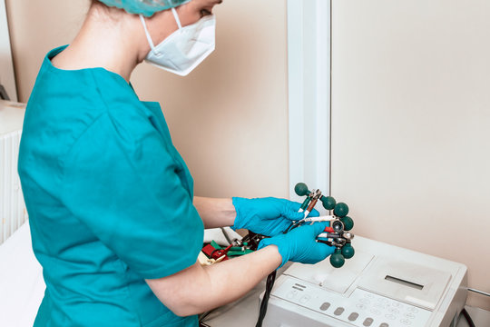 Medical professional in surgical blue uniform holding electrodes of ECG machine