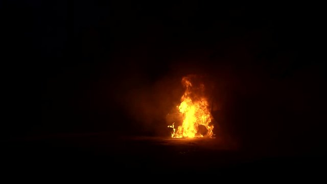 Burning car door isolated on a black background in smoke. Theme of criminal revenge and set fire to someone else car. Automobile engulfed in flames of fire. Trees close to burning sedan.