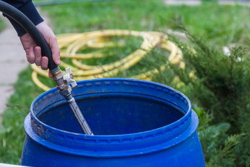 Cropped Hand Filling Water With Hose In Plastic Barrels
