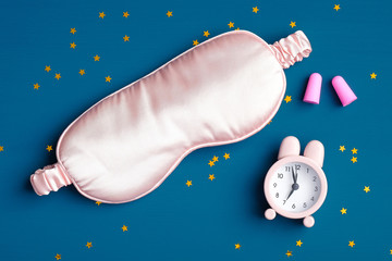 Healthy sleeping concept. Sleep eye mask, alarm clock, ear plugs on dark blue background. Flat lay,...