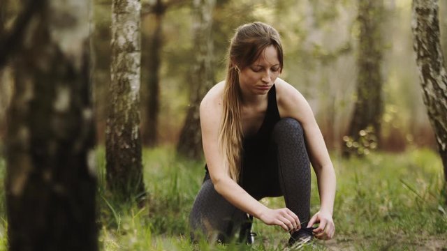 Young caucasian woman runner tying shoelace in the forest. Slow motion. Copy space