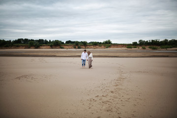 Love story of a woman and a man. Loving couple walk along the sandy Bank of the River. Concept of feelings and emotions. Young man in a white shirt and a girl in a chic long dress.