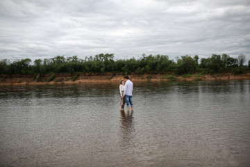Fototapeta na wymiar Сouple in love stand in the water. Hugs and kisses of men and women. The concept of love and relationships. A young couple walking along the river Bank.
