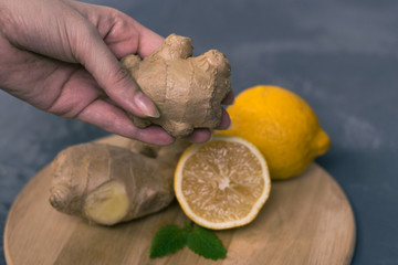 fresh ginger root with a lemon in a woman hands and mint or mellis leaves on a gray background and...