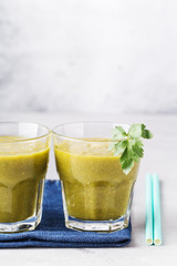 Green smoothies in glass with parsley leaf on denim napkin, gray background. Health content, healthy diet. Vertical format