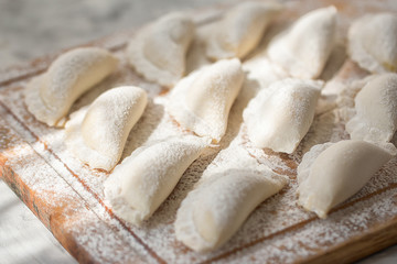 Raw dumplings on a wooden board on grey table in the morning sun.  The process of making dumplings. Close up.Top view