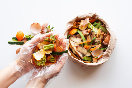 Organic food waste in paper bag and in hands on white background top view. Vegetable peelings and food leftovers ready to compost. Environmentally responsible behavior, recycling waste concept.