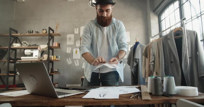 Bearded hipster fashion designer is wandering around his office, looking for inspiration for new collection - fashion, small business concept 4k footage
