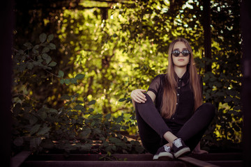 young girl in black clauses and glasses sit outside in the bushes