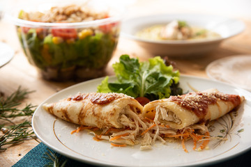 Chicken pancake on top of a white plate on a wooden table with salads in the background. Brazilian pancake