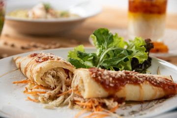 Chicken pancake on top of a white plate on a wooden table with salads in the background. Brazilian pancake