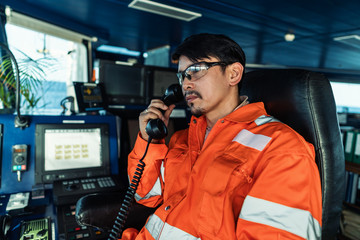 Filipino deck Officer on bridge of vessel or ship wearing coverall during navigaton watch at sea ....