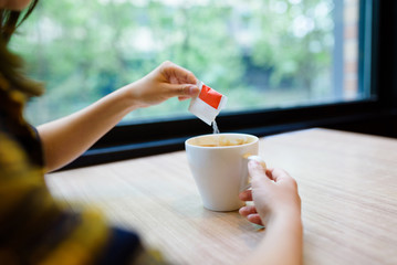 Woman pouring sugar into coffee.