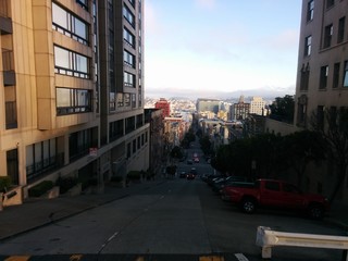Downtown San Francisco California USA - A downhill and steep city street in downtown San Francisco, with cars, a blue sky, and the cityscape in the background.