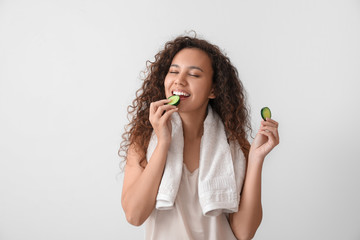 Beautiful young African-American woman with cucumber slices on light background