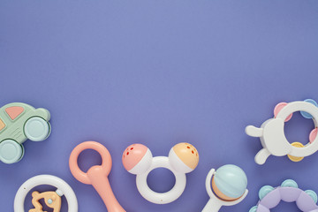 Flat lay composition with baby rattles set in pastel colors and space for text on lilac background.