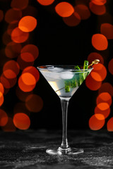 Glass of tasty cucumber martini on dark background with blurred lights